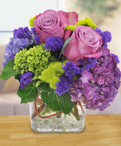 Purple Perfection features lovely lavender roses, purple and green hydrangeas and purple statice, along with green pompons and curly willow tips in a glass cube in Rockville MD, Palace Florists